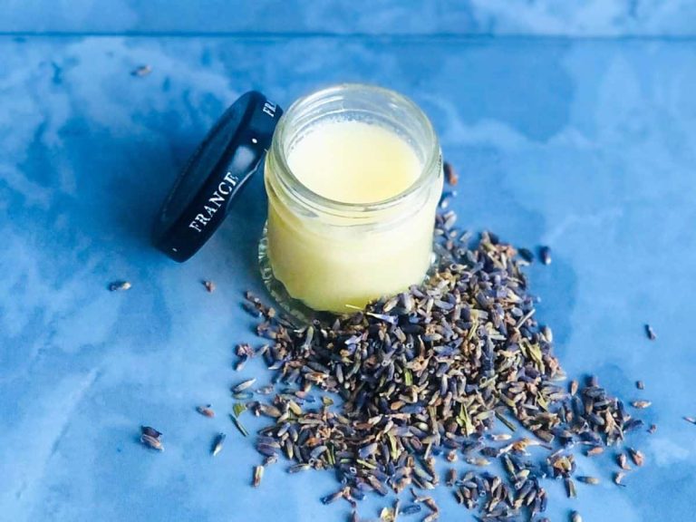 A handmade cacao butter lip balm in a repurposed jam jar against blue tiles.