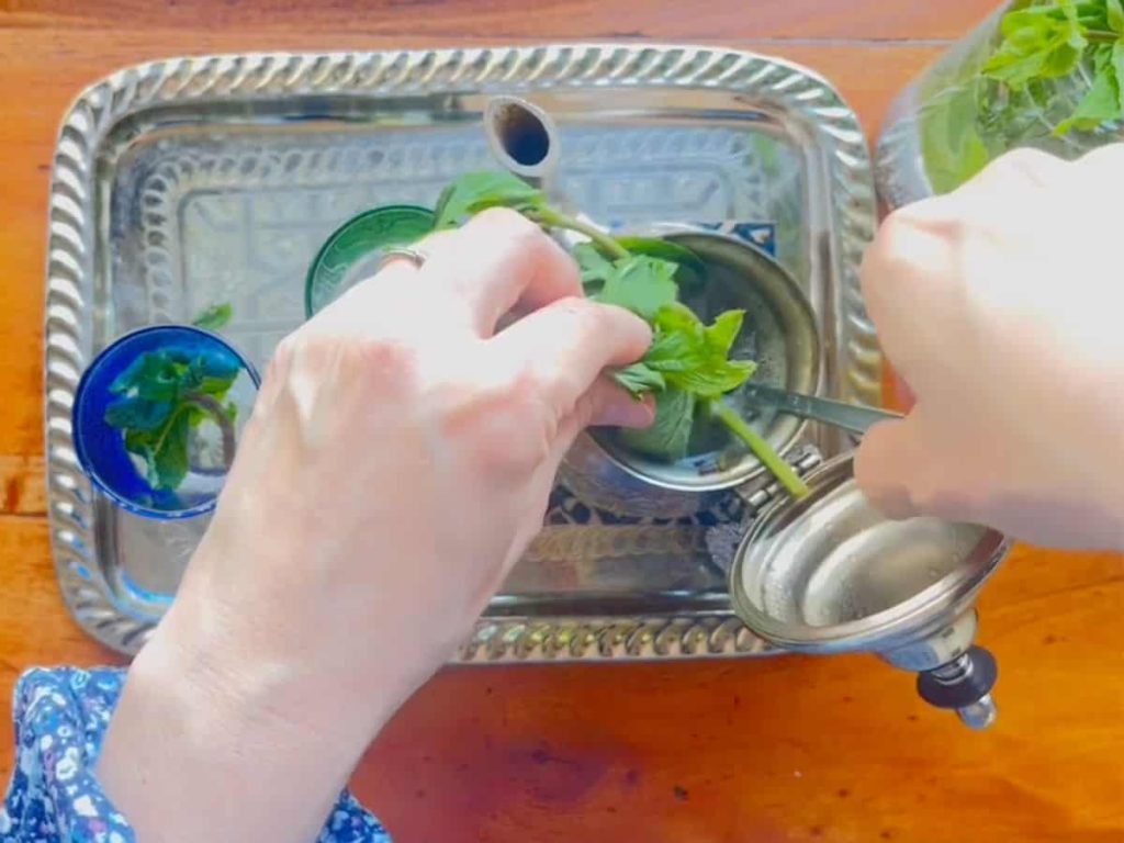 A woman is adding a bouquet of Moroccan mint to the tea kettle.