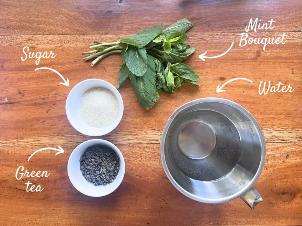 The ingredients for Moroccan mint tea on the table: a bouquet of mint, loose green tea, water, and sugar.