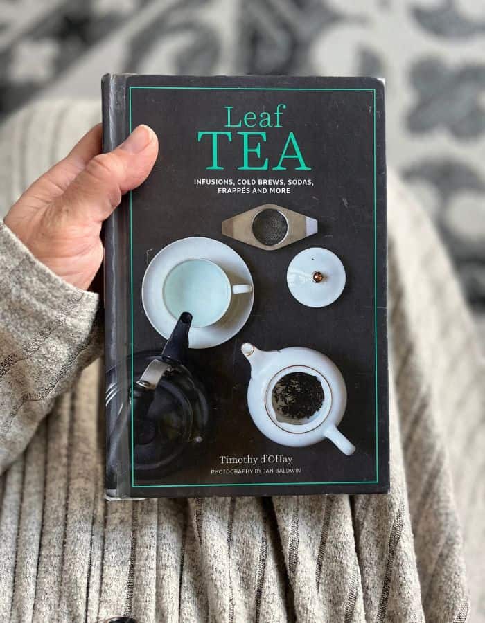 A woman is holding in her hand one of the best books about tea and infusions: the Leaf TEA by Timothy d'Offay.