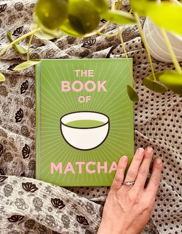 Best matcha tea book on the fabric surface and a hand of the woman is grabbing the corner to turn the page to start to read.