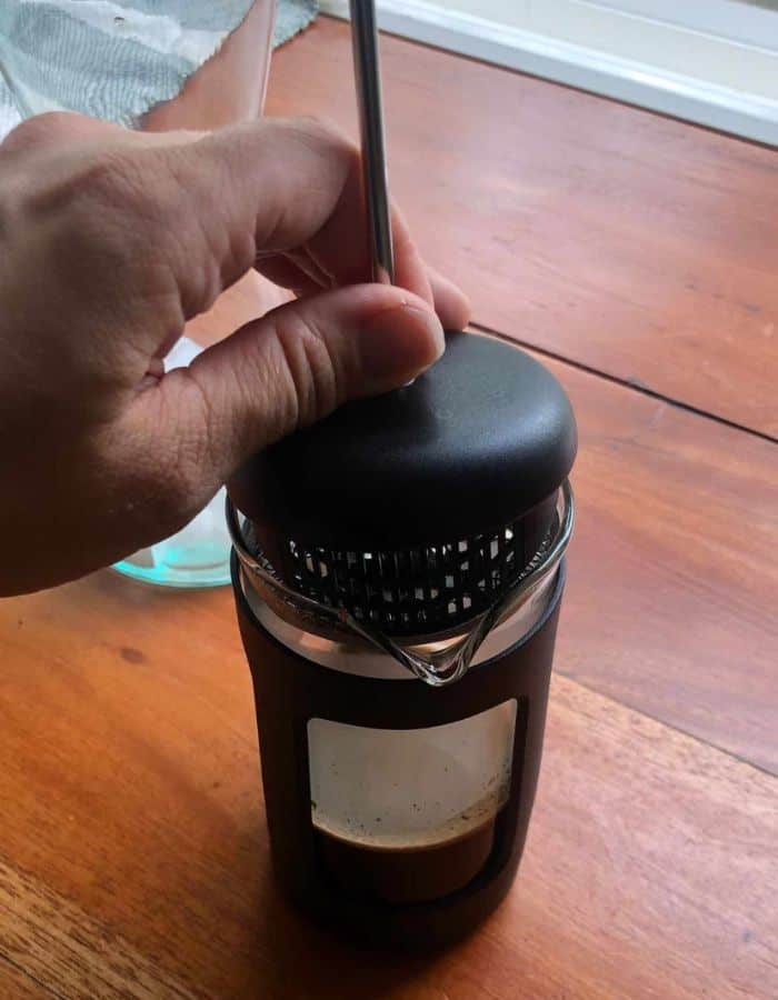 A woman is placing the plunger into the French press.