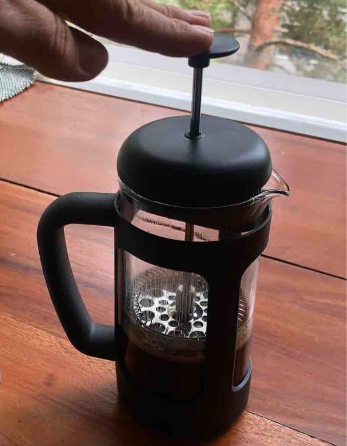 A woman is pushing down the plunger in the French press to make Moroccan Spiced coffee.