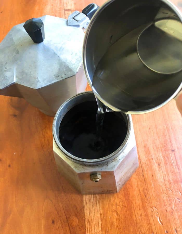 A woman pouring water into the bottom part of the Italian coffee maker.
