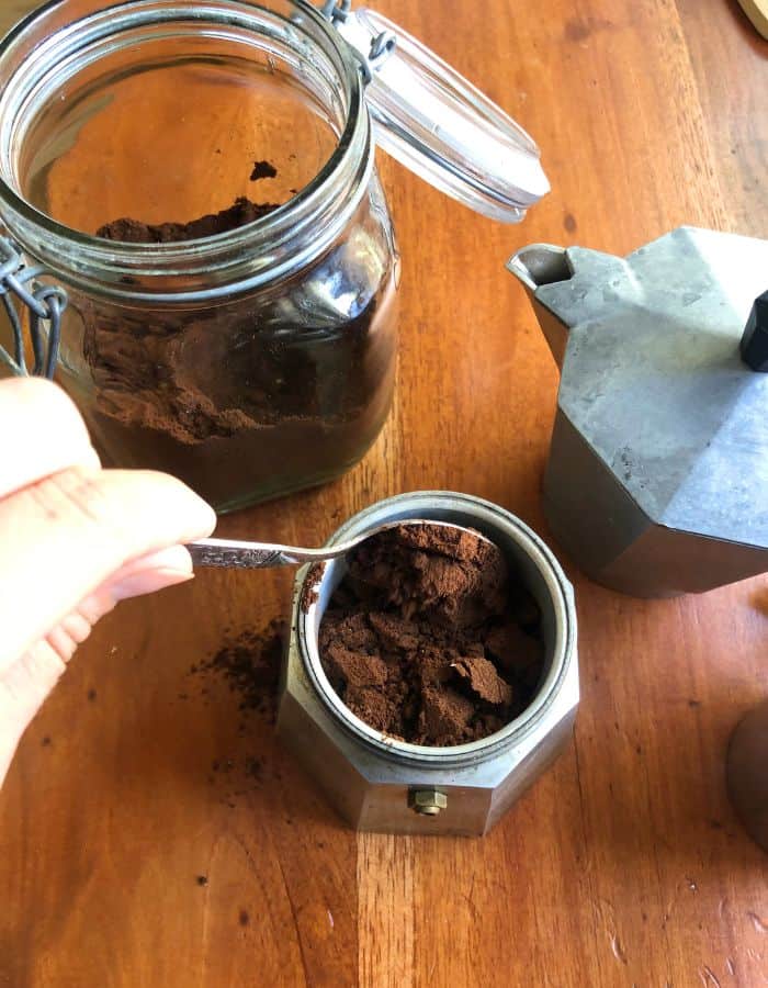 A woman measuring Moroccan spiced coffee grounds into the coffee strainer basket of an Italian coffee maker.
