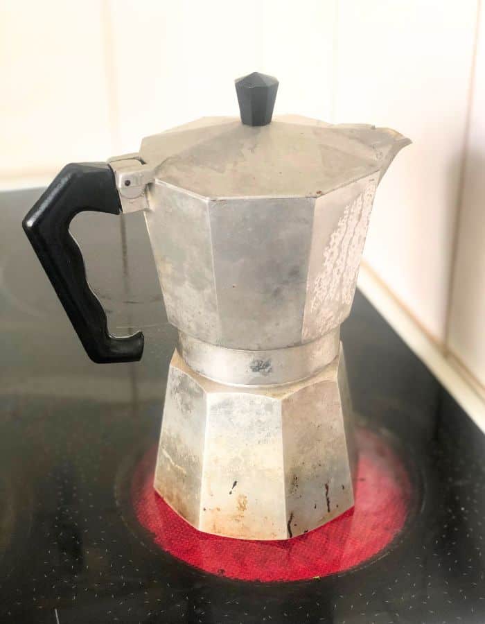 An Italian coffee maker brewing Moroccan spiced coffee on the stove that is on.