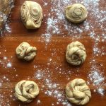 On a wooden surface some twisted buns, rolled buns, and knotted buns made from cinnamon roll dough.