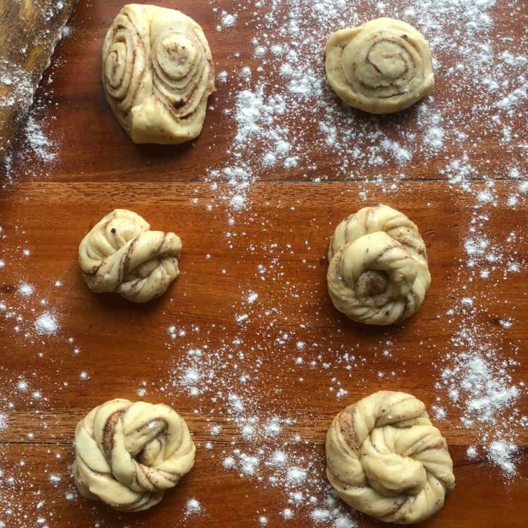 On a wooden surface some twisted buns, rolled buns, and knotted buns made from cinnamon roll dough.