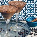 Two cocktail glasses of Moroccan Coffee Cocktail with chocolate rim standing on a silver tray with coffee beans sprinkled around.