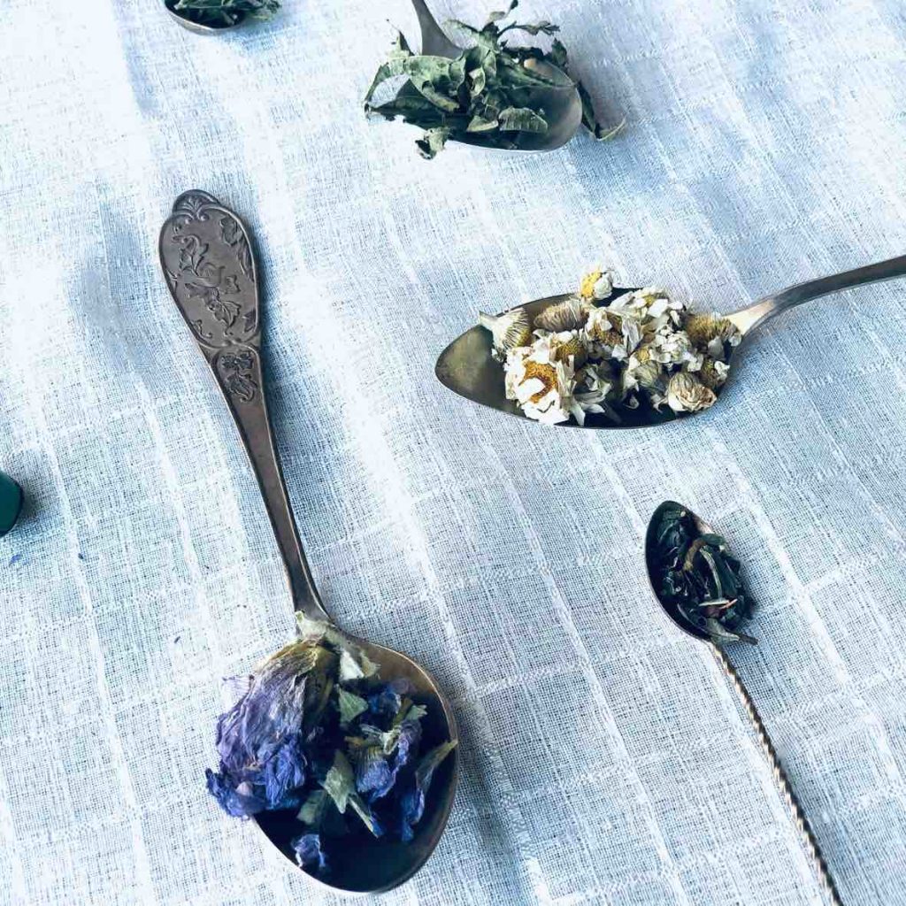 Spoons on a white linen filled with dried herbs for tea.