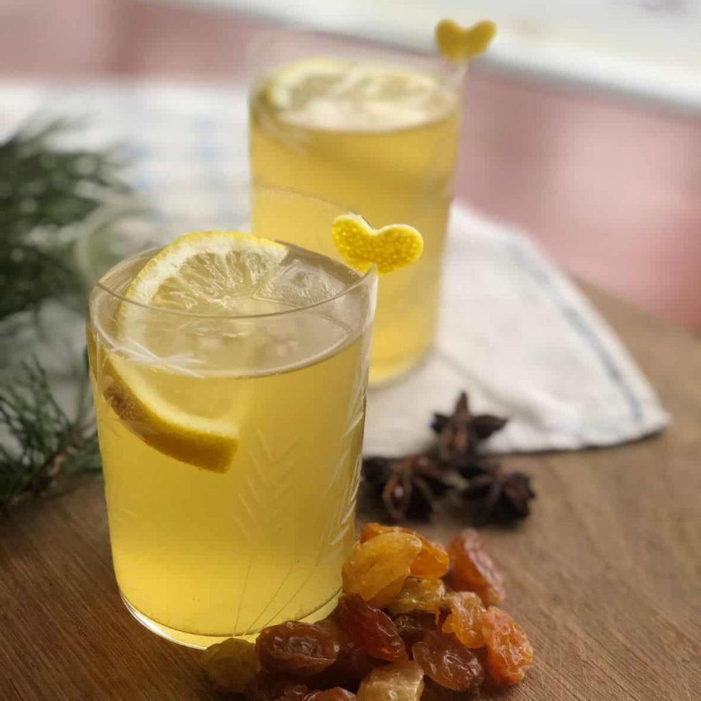 White glogg with elderflower and citrus poured in the glasses and decorated with lemon slices and lemon peel, with some golden raisins on the side.