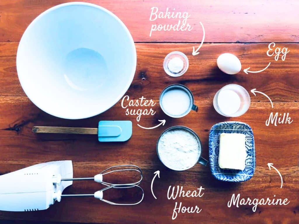 Ingredients for blueberry pie on a wooden surface: Wheat flour, margarine, caster sugar, milk, egg, and baking powder.
