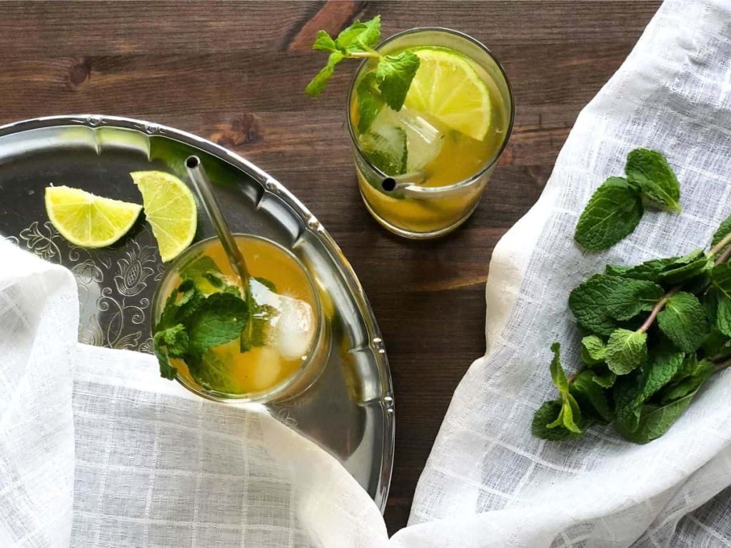 Iced Moroccan mint tea served in the glasses with some lime slices on a silver tray.