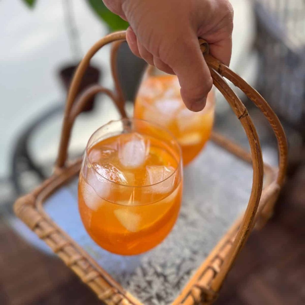 Two Riedel O glasses filled with rooibos iced tea on a tray that a hand is holding.