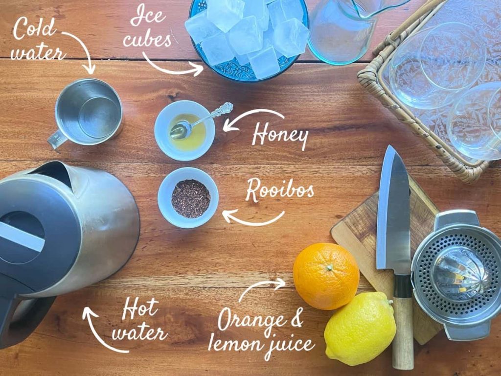 The ingredients of rooibos iced tea on the wooden surface: rooibos  leaves, honey, cold and hot water, ice cubes, orange and lemon juiced.