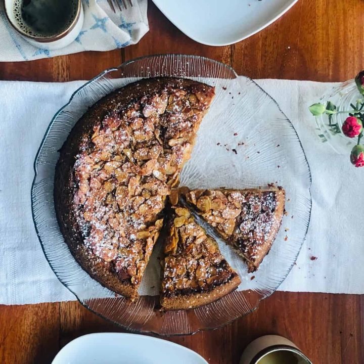 Tosca cake cut in several serving pieces on a glass serving plate on a dining table.
