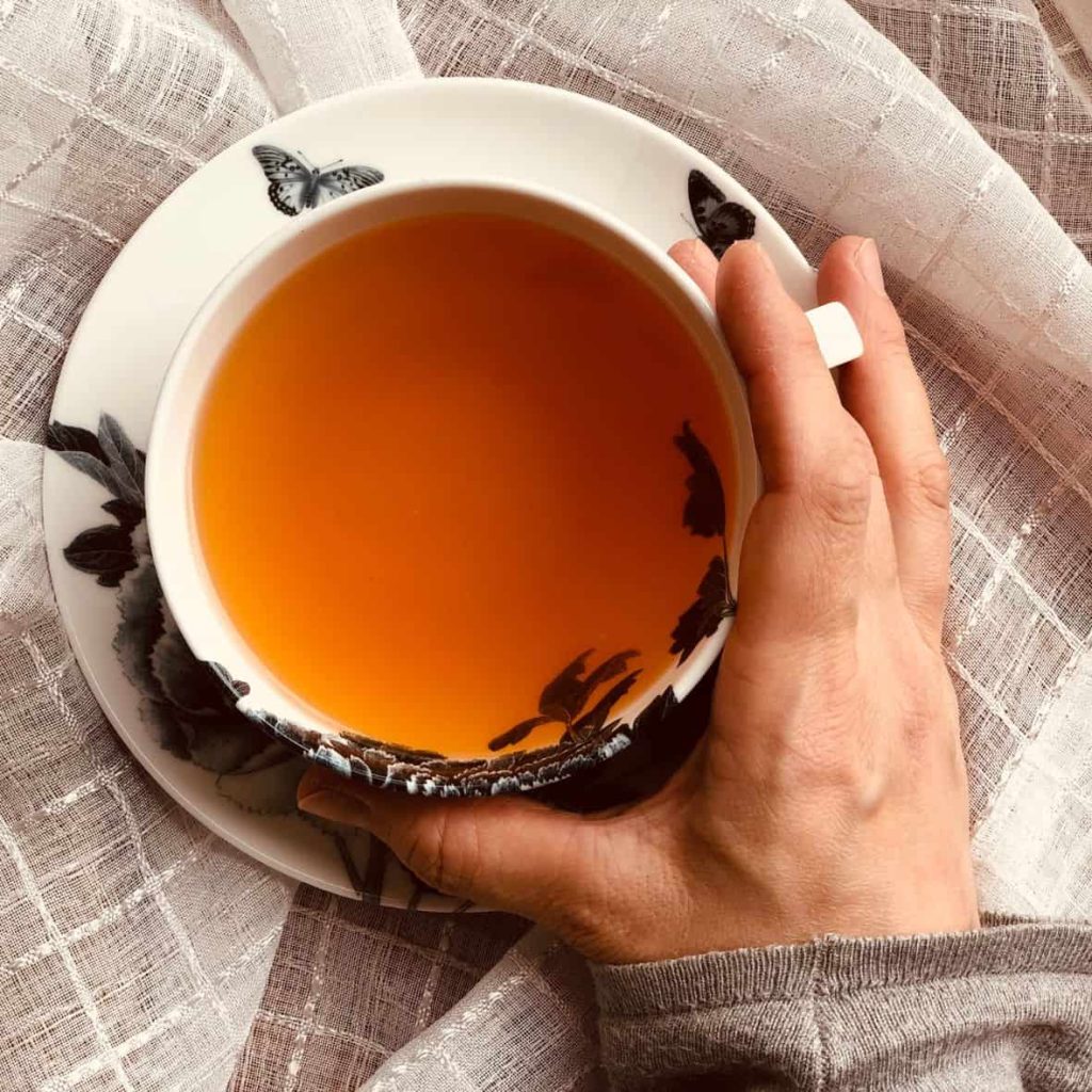 Natural wellbeing moment: woman holding a tea cup of rooibos tea in a ceramic cup decorated with leaves and butterflies