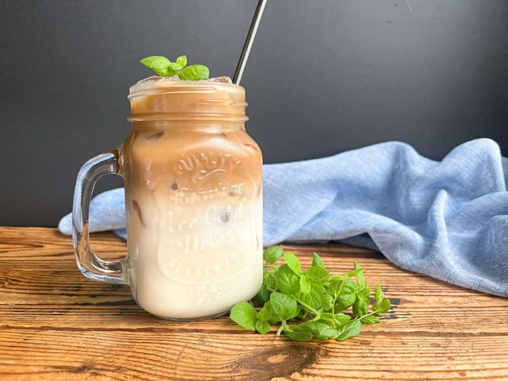 Iced latte with homemade mint simple syrup decorated with mint sprigs and metallic straw.