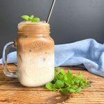Iced latte with homemade mint simple syrup decorated with mint sprigs and metallic straw.