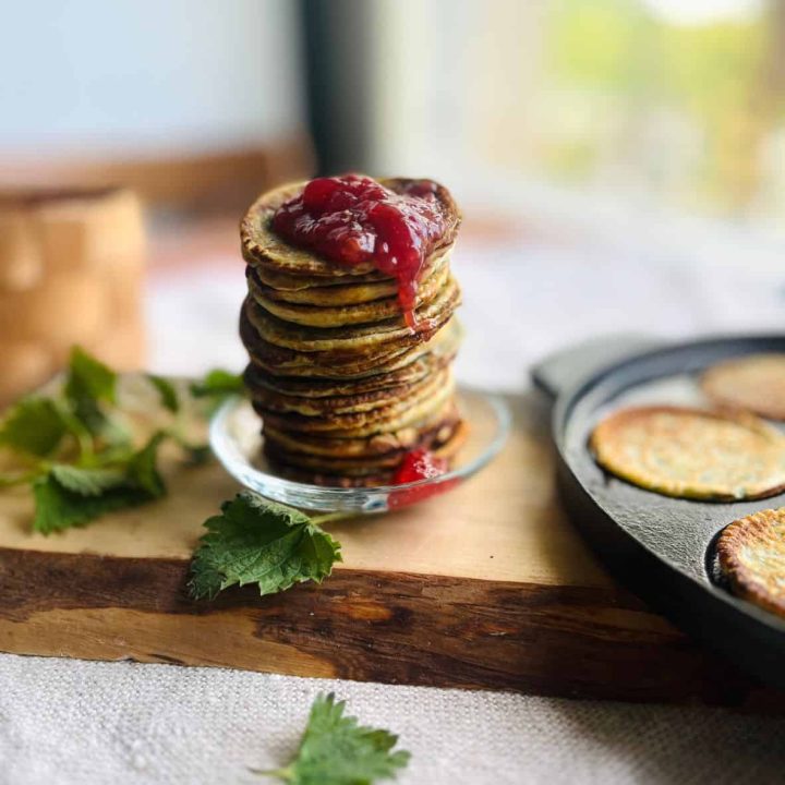Homemade nettle crepes on a pile with some raspberry jam dripping down.