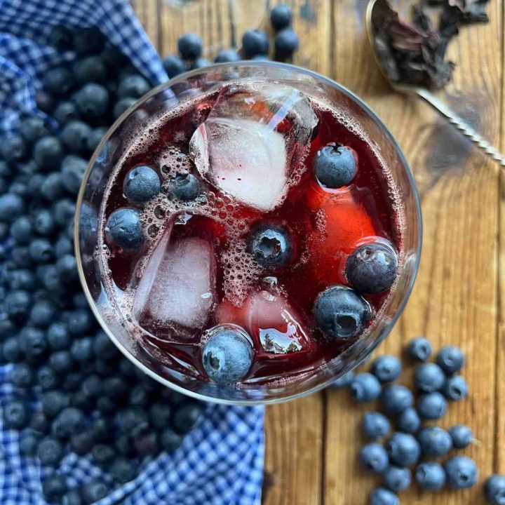 From above: a glass full of blueberry hibiscus iced tea and served with ice and fresh highbush blueberries.