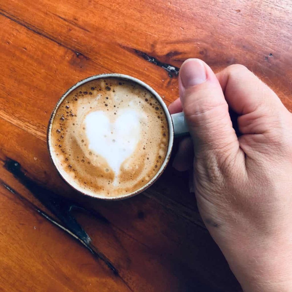 A woman holding a cappuccino with a heart latte art on it as a soft morning ritual.