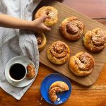 Homemade kanelsnegle buns the Danish cinnamon swirls on a wooden serving board, and a girl is grabbing one of the buns.