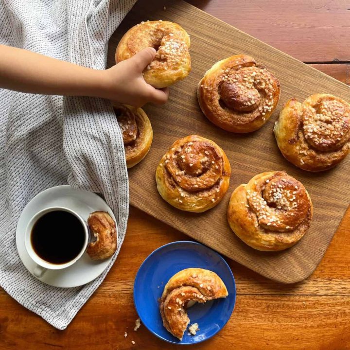 Homemade kanelsnegle buns the Danish cinnamon swirls on a wooden serving board, and a girl is grabbing one of the buns.