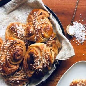 Traditional Finnish Cinnamon Buns, Korvapuustit, on a serving tray with some pearl sugar sprinkled on the the top and on the table.