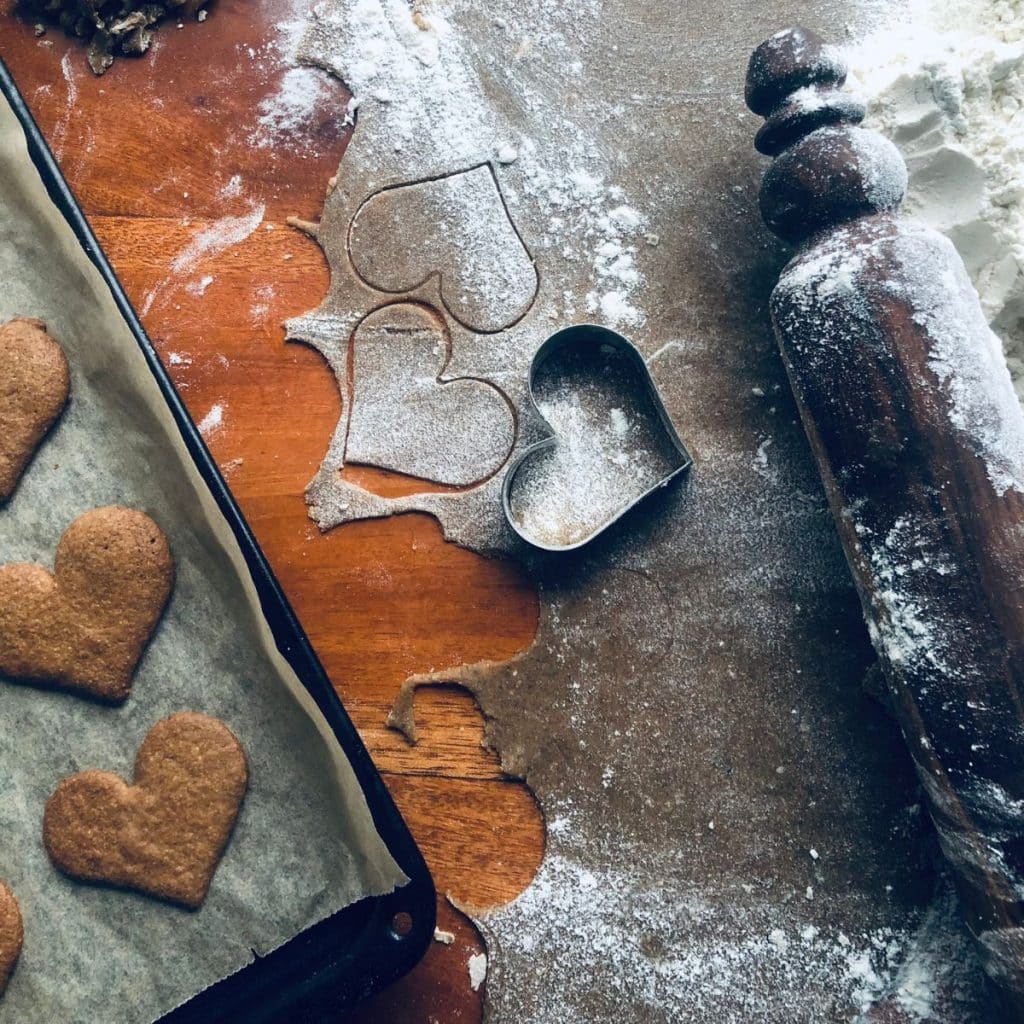 Spiced rye ginger breads in making: some on a baking tray, som outrolled dough on the table with cookie cutter and rolling pin.