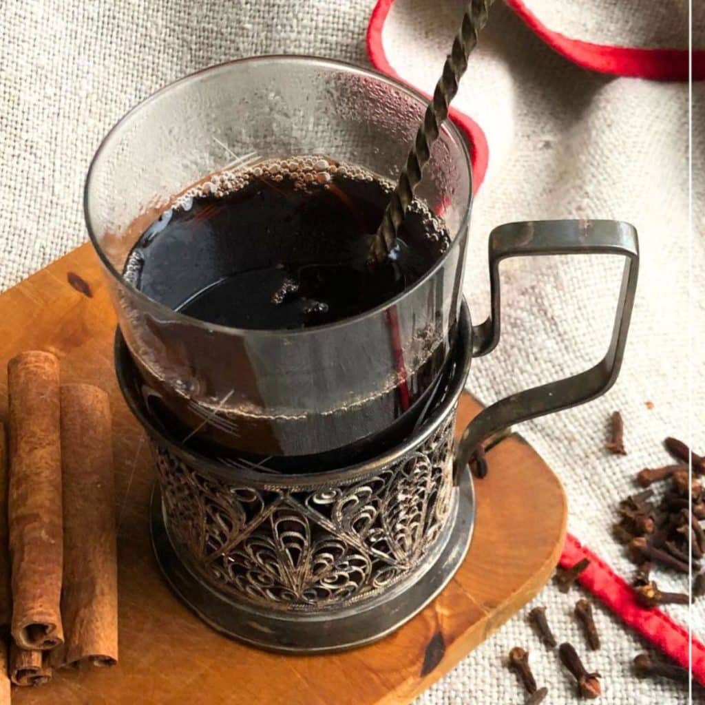 Traditional red glogg in a Nordic glogg glass with some cinnamon sticks and cloves on the side.