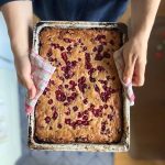 A woman holding a square pie tin with lingonberry pie fresh from the oven.