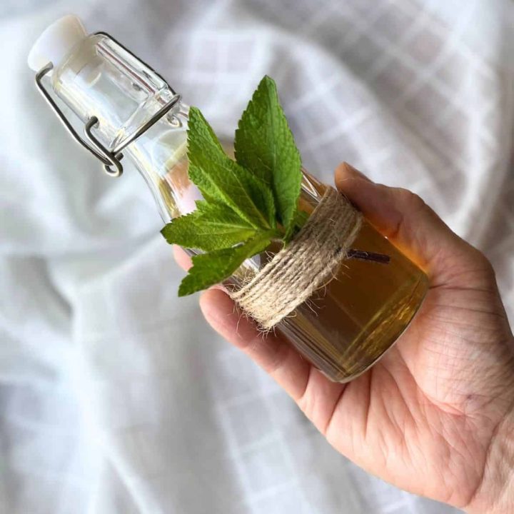 Mint simple syrup in a glass bottle and a woman holding bottle in her hand.