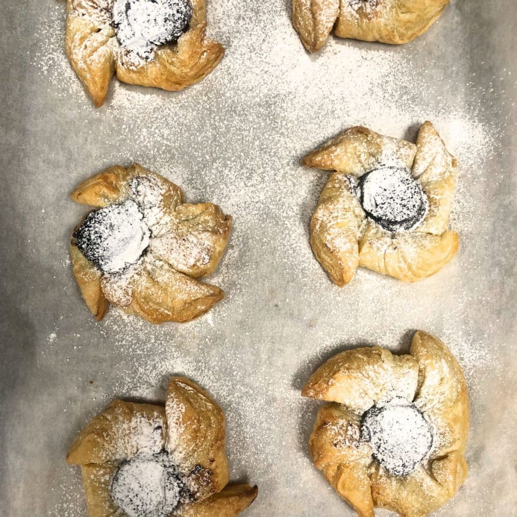 Plum pinwheel tarts,Nordic Winter and Christmas time treats, on a baking paper and dusted with powdered sugar.