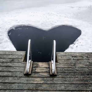 Cold plunge and winter swimming place in a sea with wooden pier, metallic stairs and an ice hole in the frozen sea.