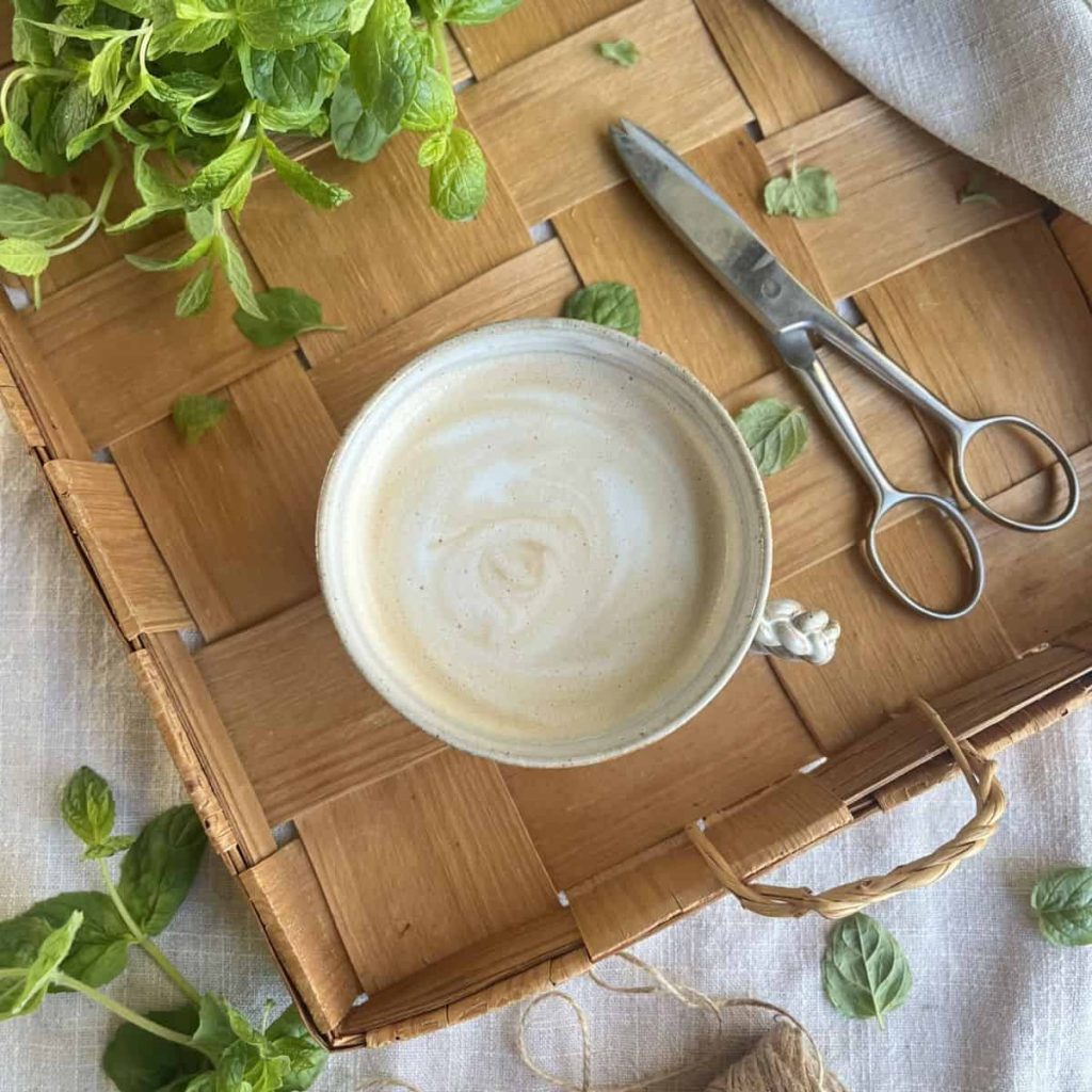 Mint latte made with fresh homemade mint syrup, with a mint bush and scissors on the wooden tray.