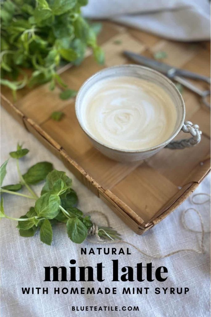 Natural mint latte in a ceramic cup on a wooden tray with fresh mint leaves on the side.