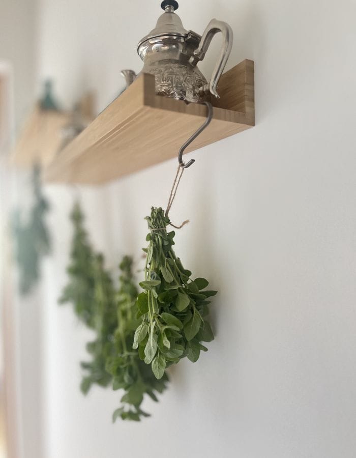 Fresh spring herbs drying from a yearn with a brass tea pot on the shelf.