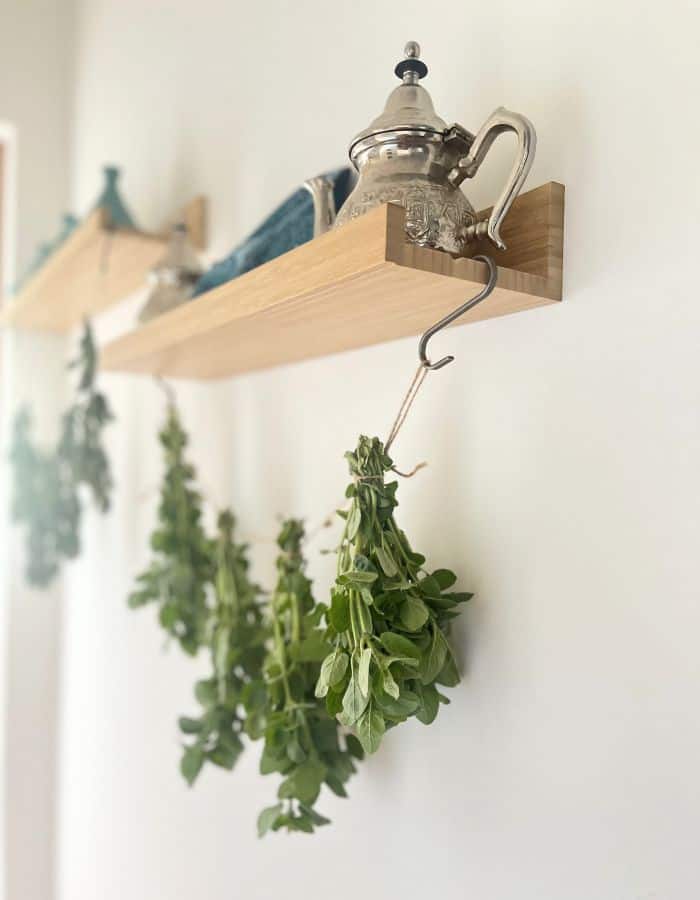 Tea herbs drying from a ribbon hanging from a shelf, where a teapot is placed.