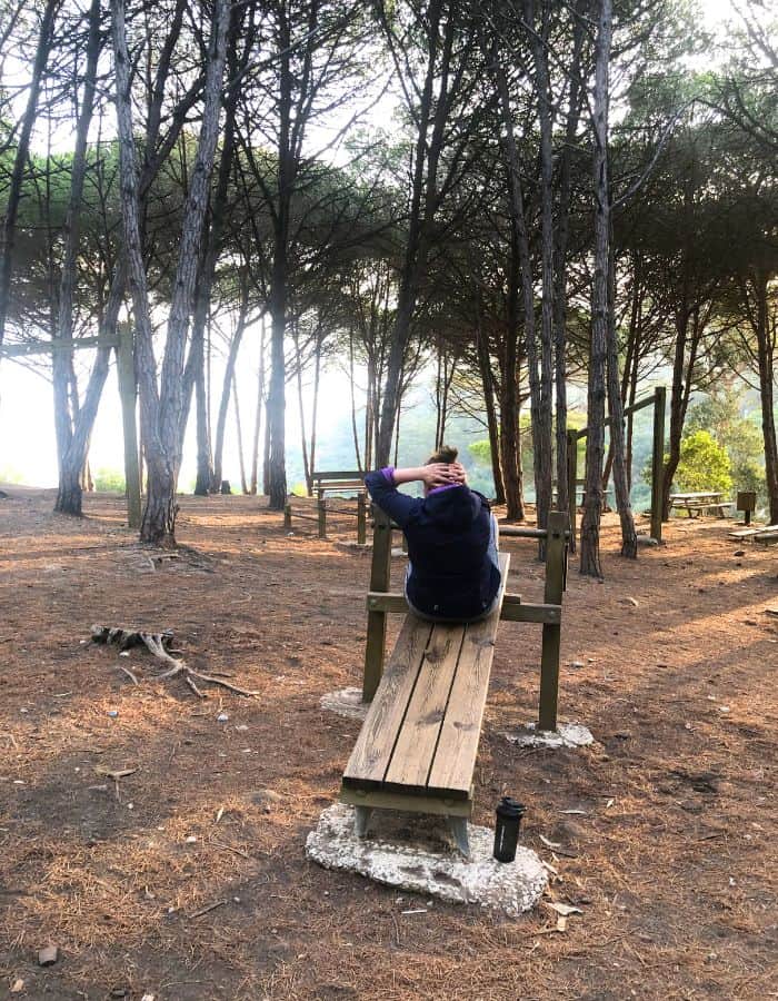A woman making sit-ups in the outdoor gym in the forest.