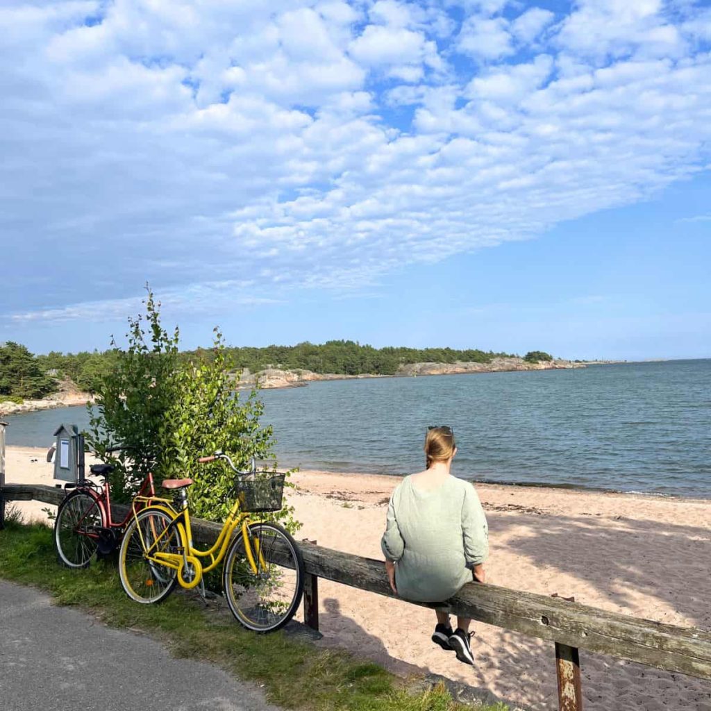 A woman by the sea shore sitting on a log and two bikes parked next to her.