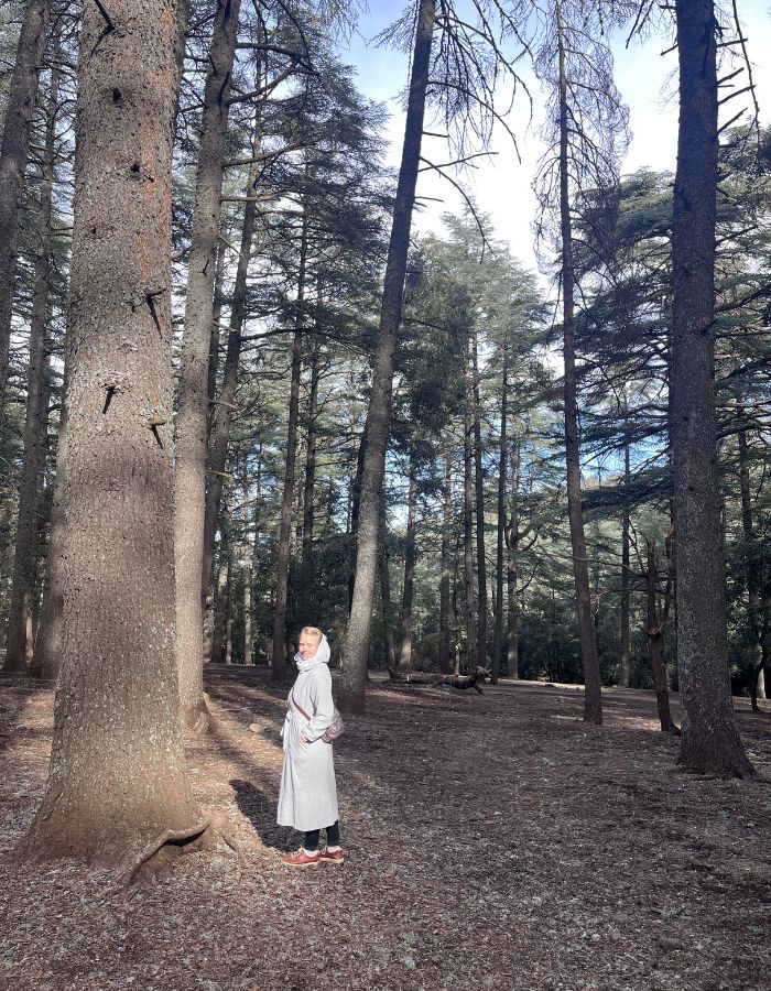 Woman in a long white jacket on a walk in a forest abroad.