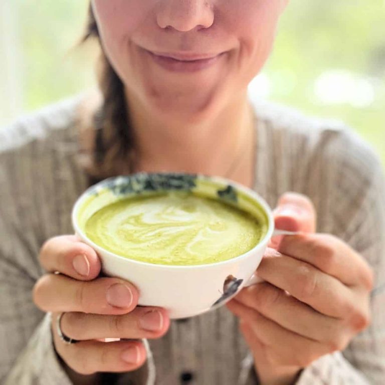 A woman holding a vanilla matcha latte in her hands smiling.