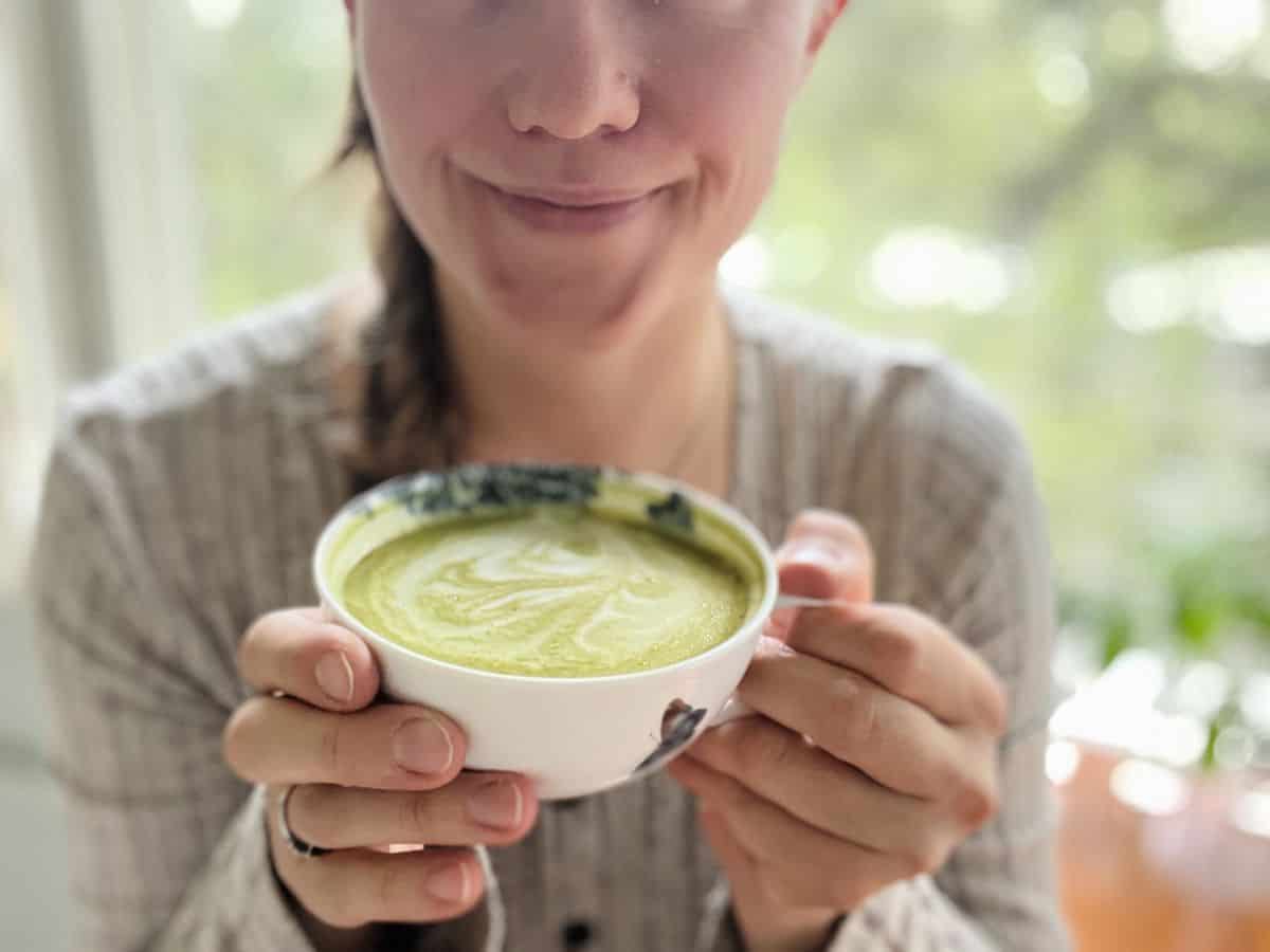 A woman smiling with a cup of homemade vanilla matcha latte in her hands.