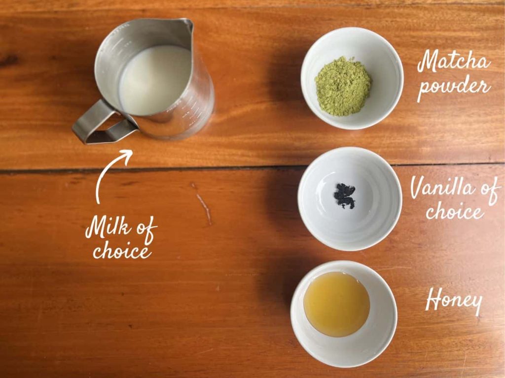 The ingredients for a vanilla matcha latte: Milk of choice, Matcha powder, vanilla of choice, and honey in tiny jars.