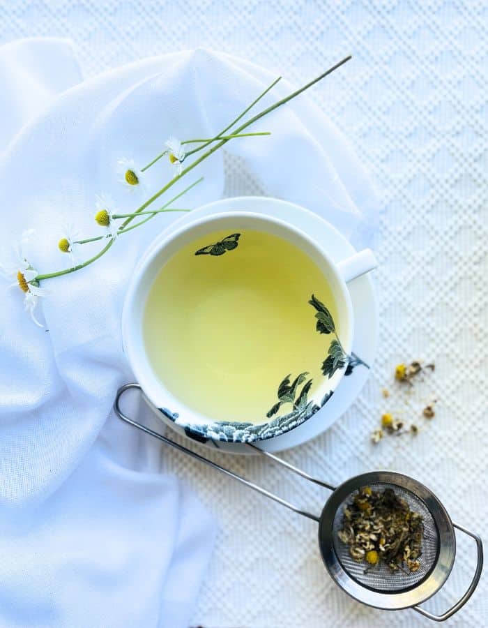 Chamomile tea in a cup and dried chamomile flowers on the side for flower tea.