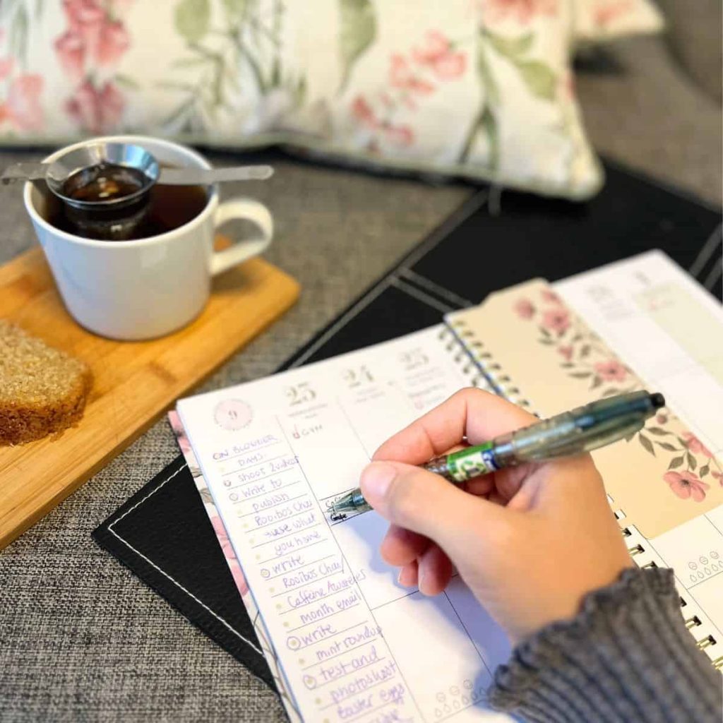 A woman is making markings in her life planner with teacup next to her.