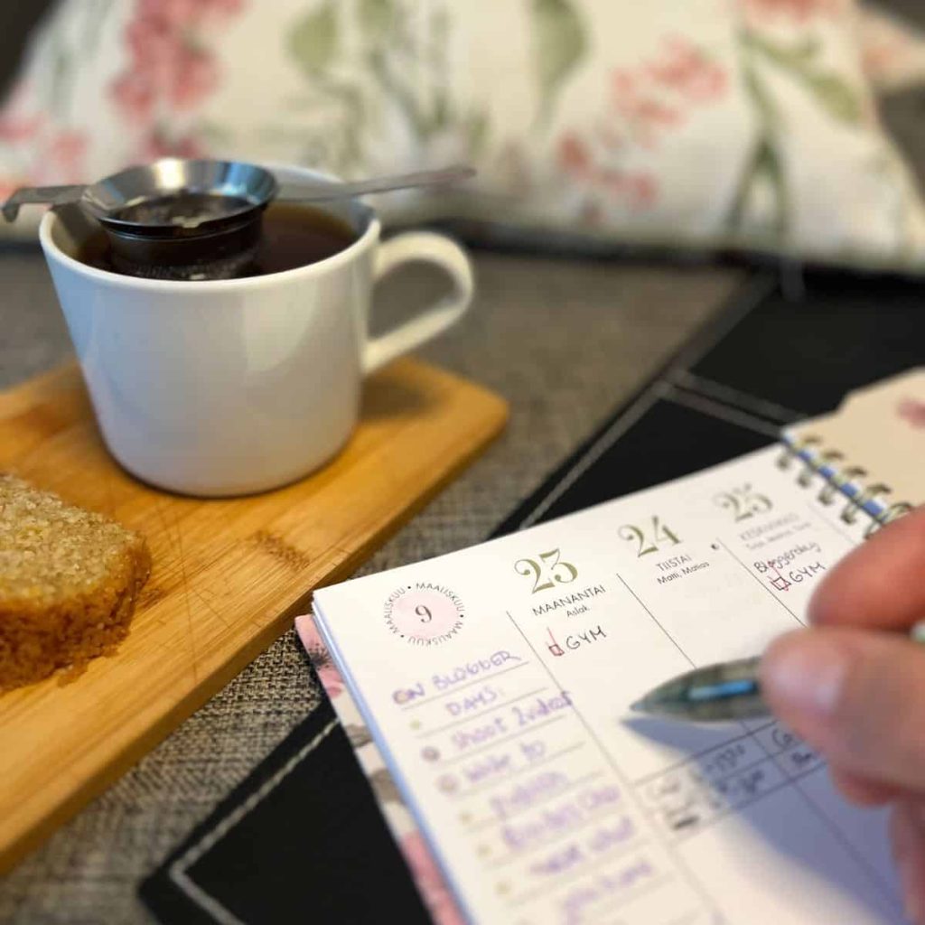 A woman marking down the gym slots of the week in her planner. A tea steeping in a white cup on the background.