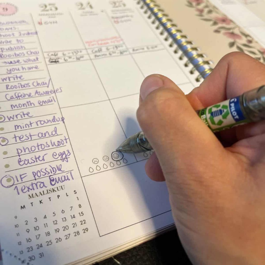 Woman is cirlicing a smiley on a emotional scale in her planner.