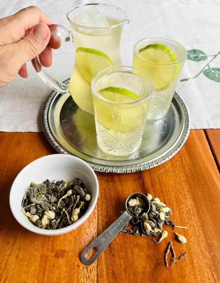 A summery iced tea tray with a glass jar and two glasses filled with iced jasmine green tea.